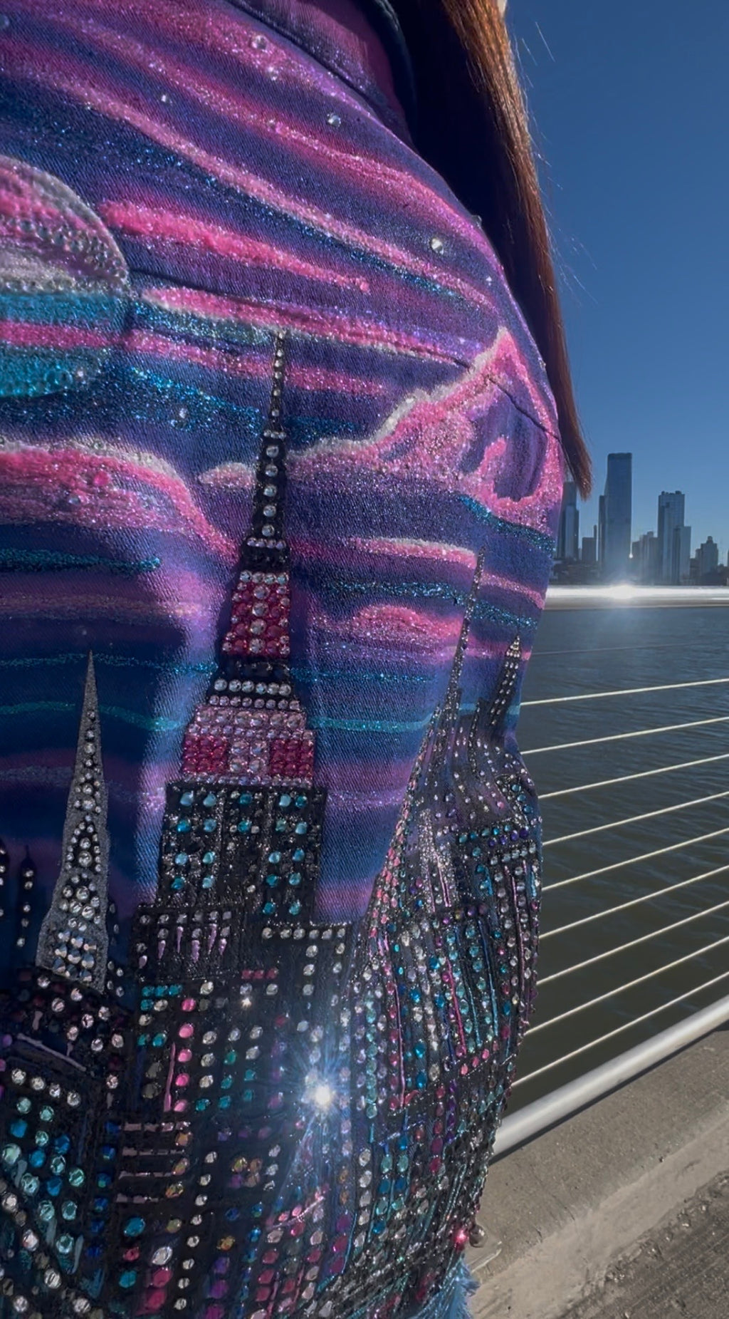 Person wearing a colorful jacket with a Loria NYC Art cityscape design against a night sky.