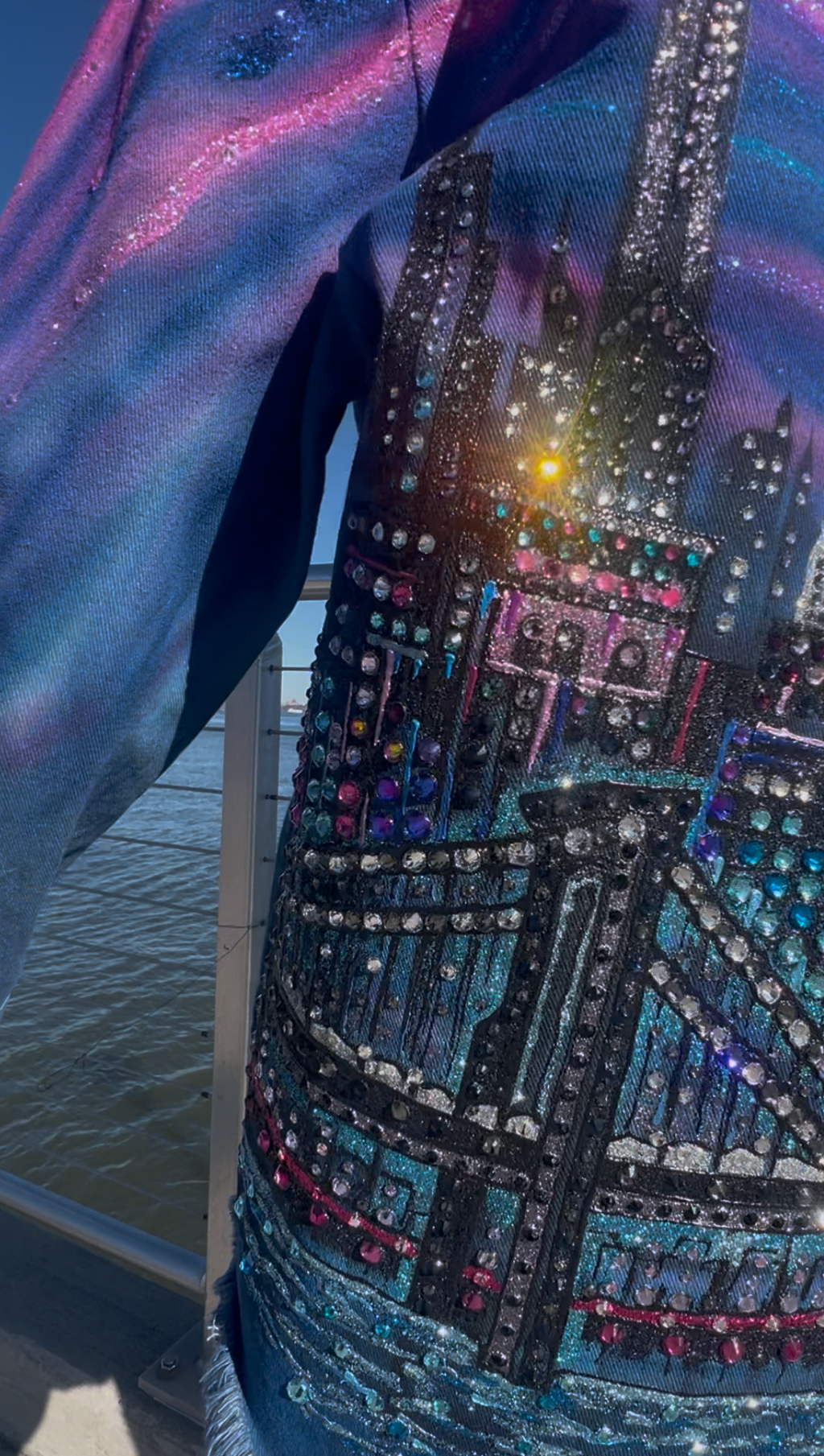 Close-up of a denim jacket with colorful embellishments and a cityscape Loria NYC Art design.