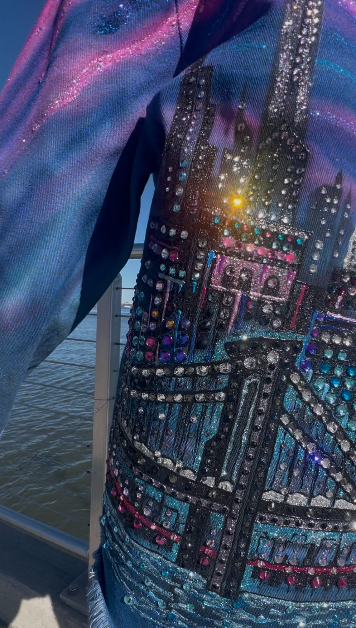Close-up of a denim jacket with colorful embellishments and a cityscape Loria NYC Art design.