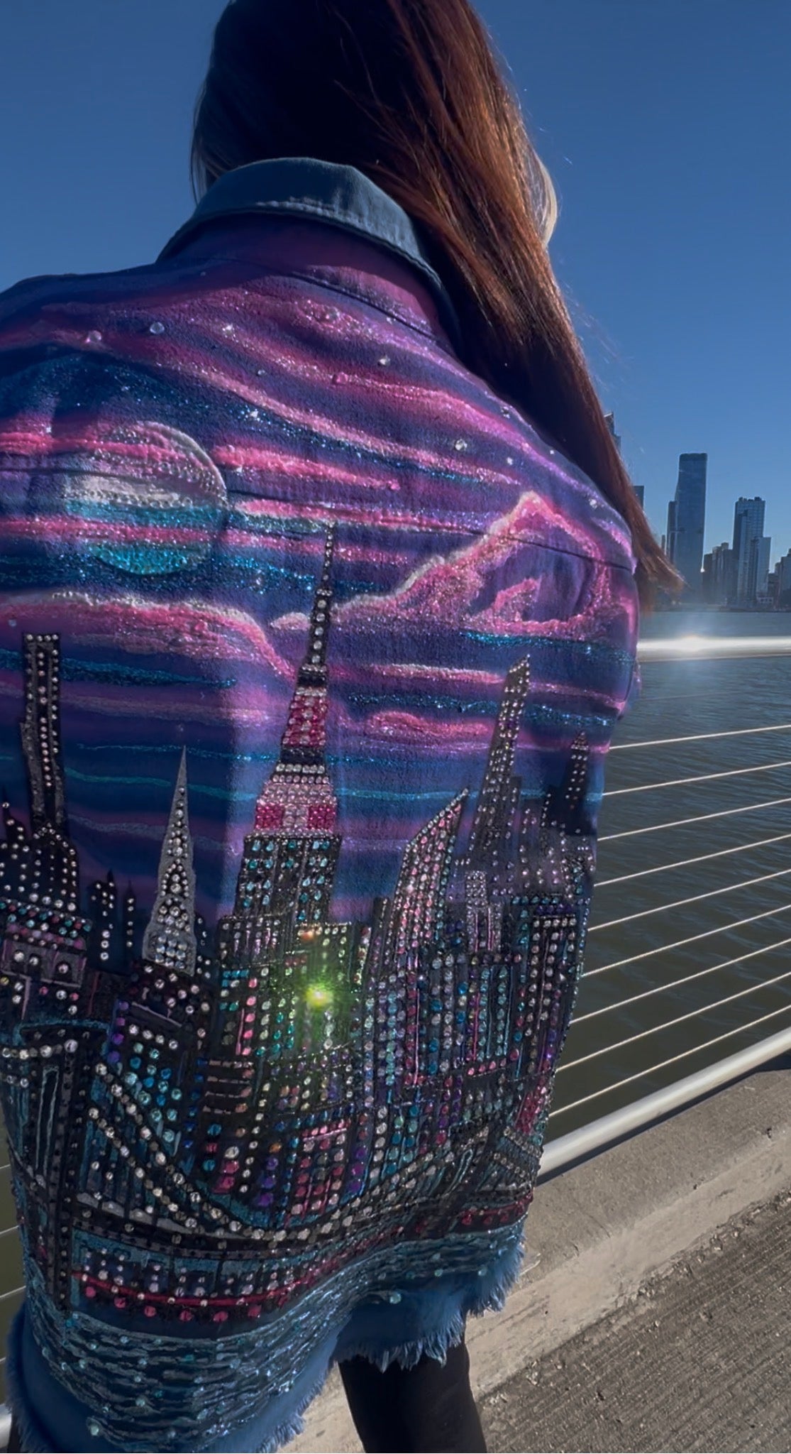 Person wearing a jacket with a Loria NYC Art cityscape design at night.