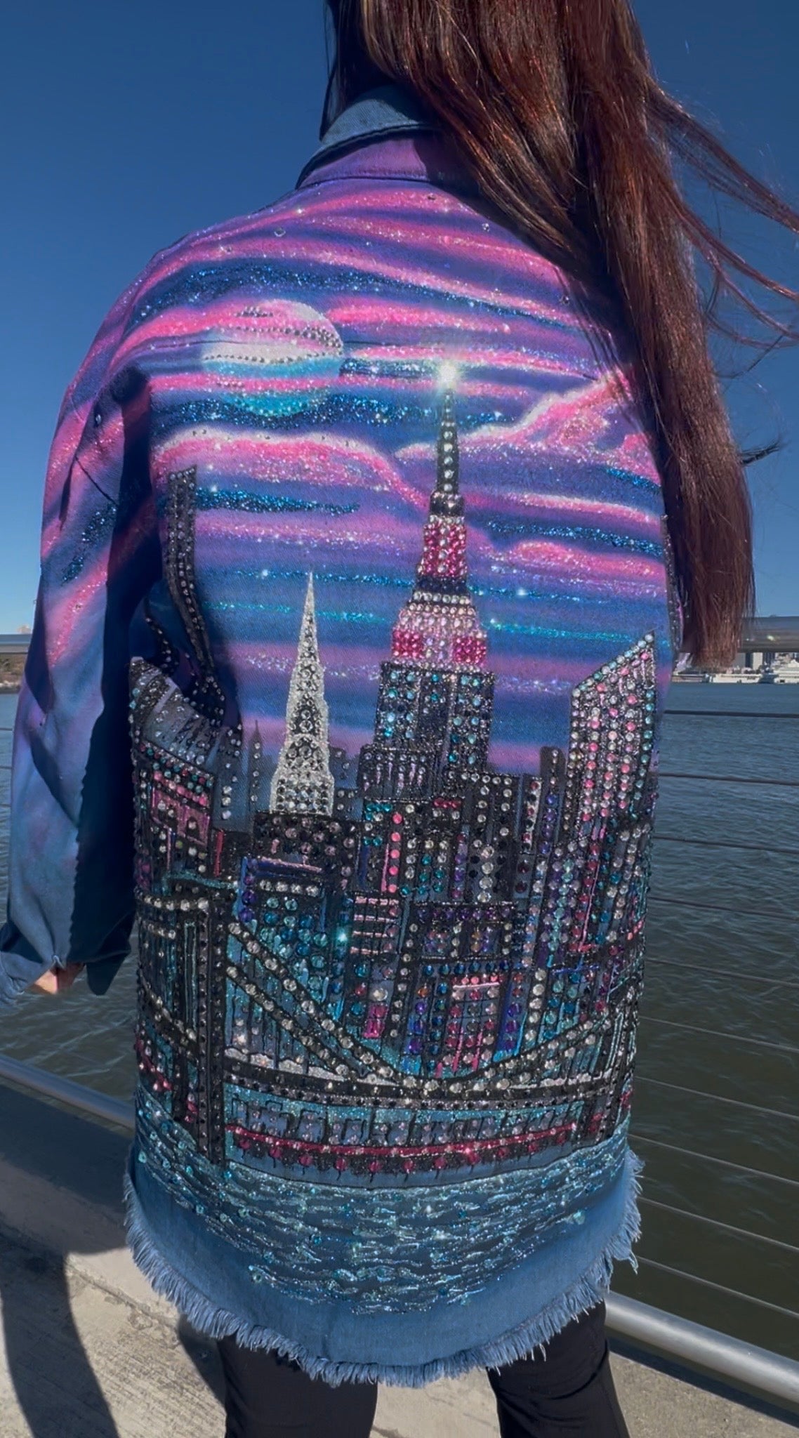 Person wearing a jacket with a Loria NYC Art cityscape design by a waterfront