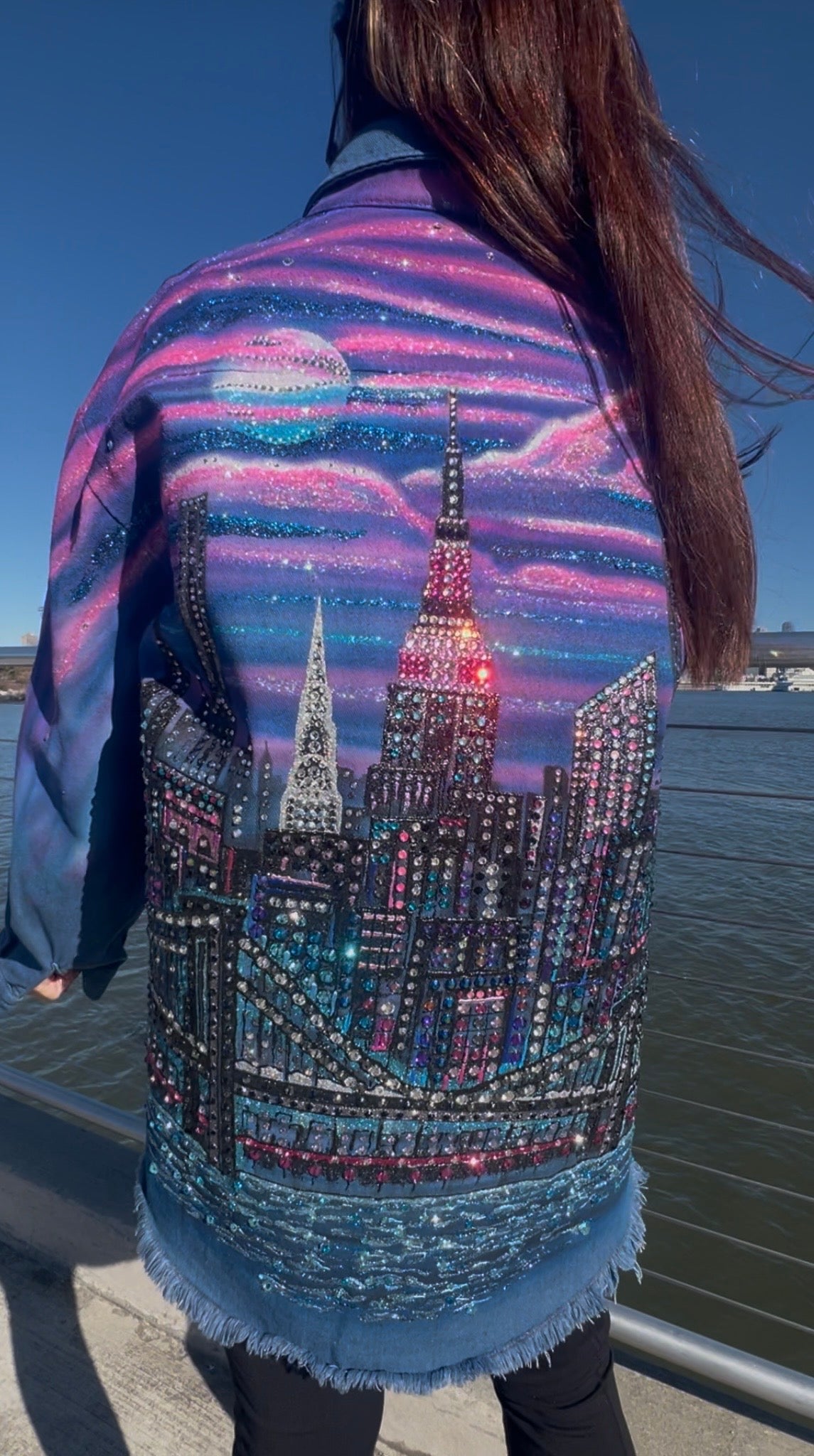 Person wearing a denim jacket with a cityscape Loria NYC Art design by a waterfront