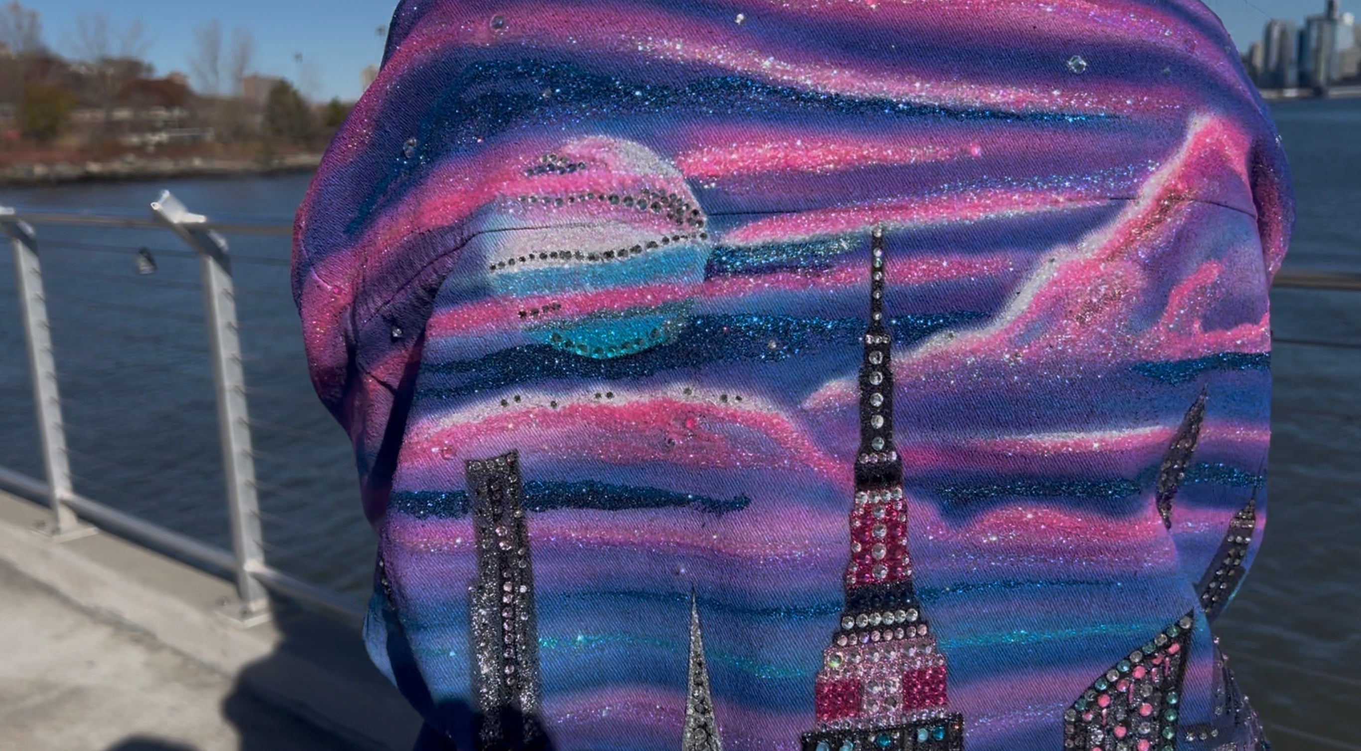 Backpack with a cityscape Loria NYC Art design featuring tall buildings, including the Empire State Building , against a blue sky. 