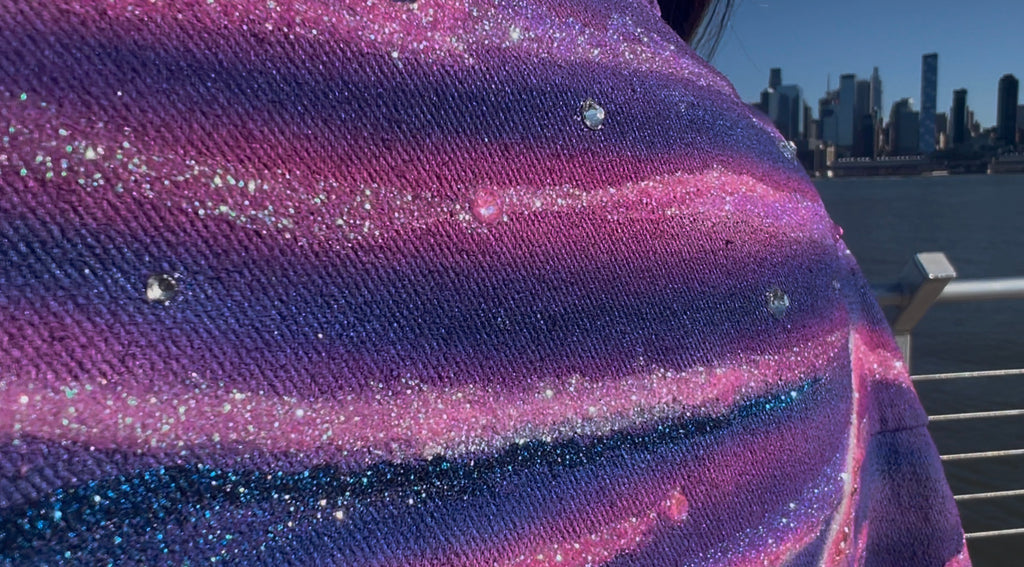 Close-up of a glittery purple fabric with a Loria NYC Art city skyline in the background