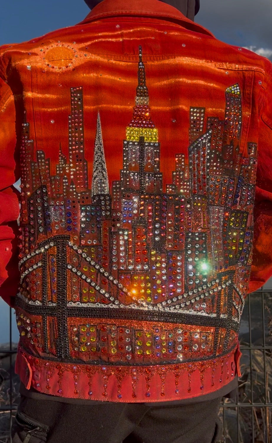 Man wearing a vibrant orange Loria NYC Art jacket with reflecting crystals.