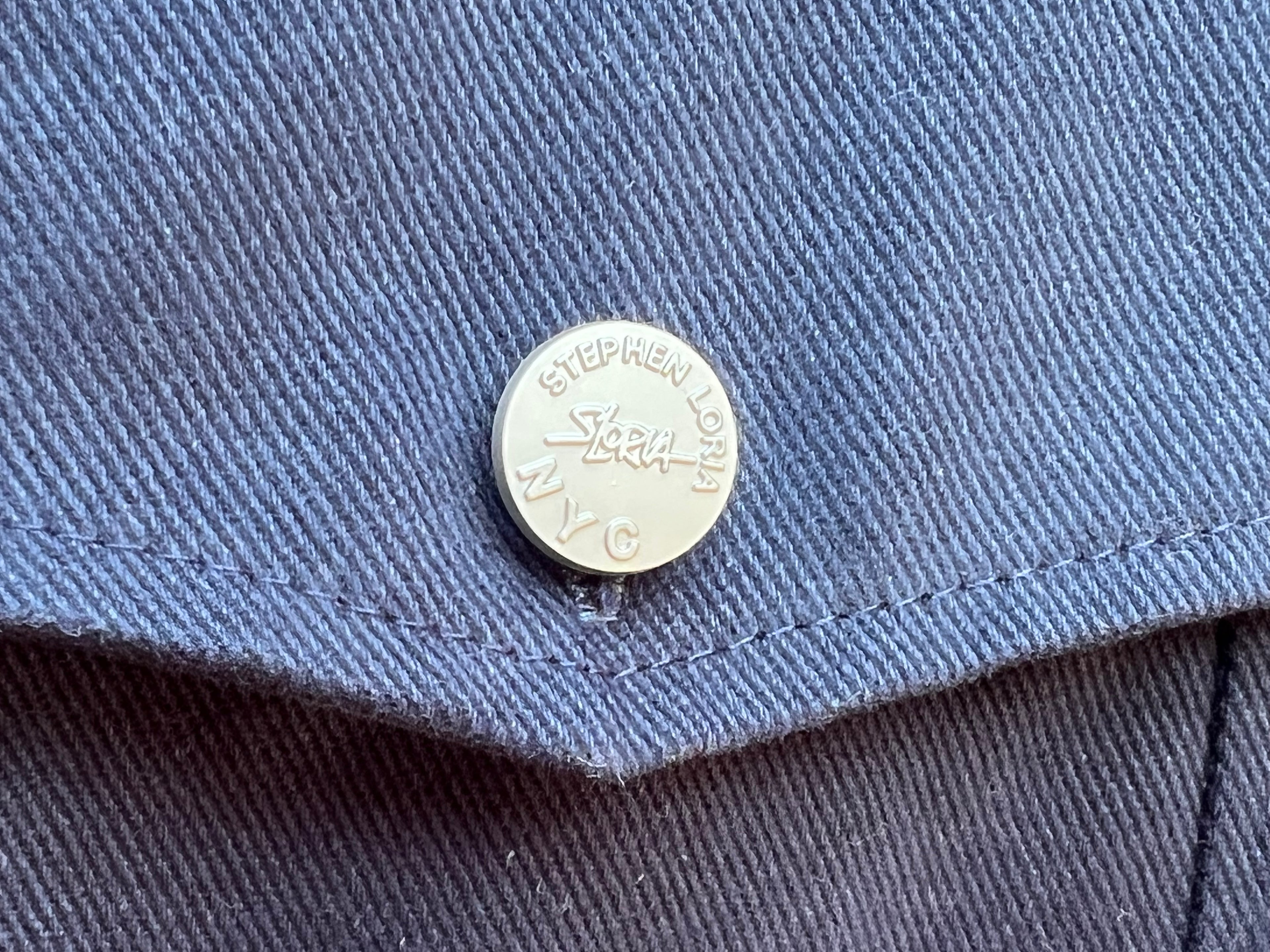 Close-up of a button on a blue garment with 'Stephen Loria' branding.