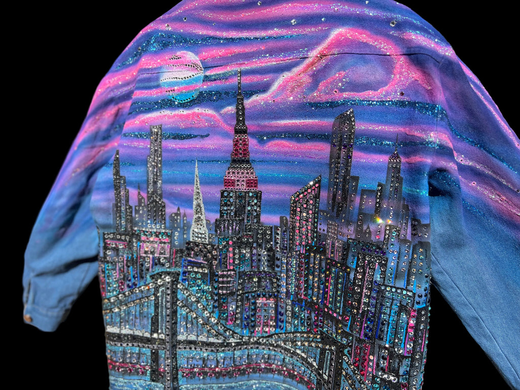 Blue jacket with a cityscape Loria NYC Art design featuring tall buildings and a bridge, set against a colorful sky.