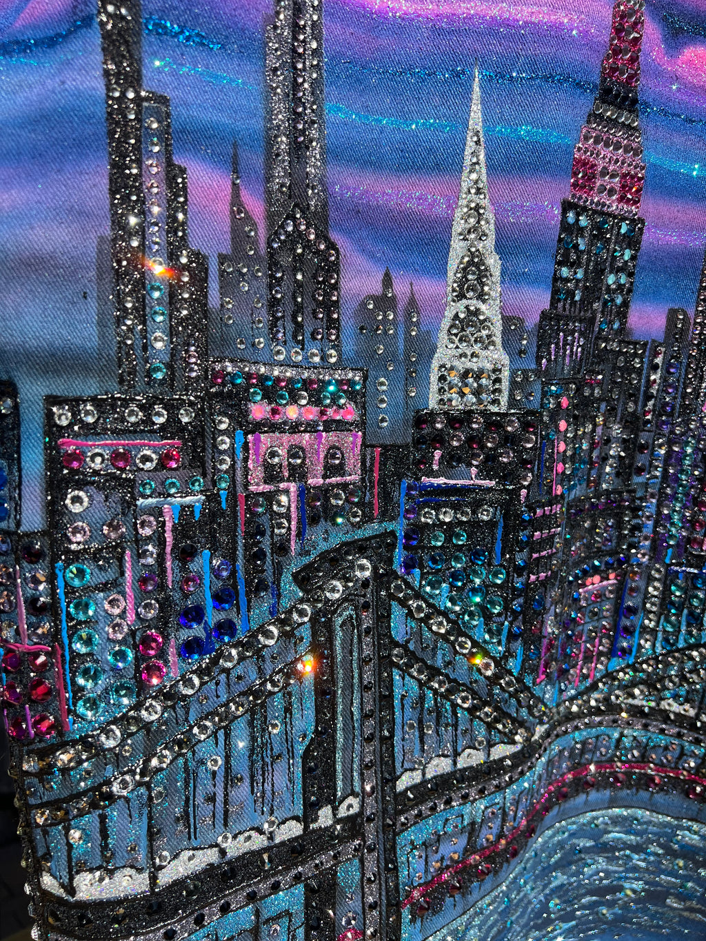 Close-up of a decorative Loria NYC Art with intricate beadwork and sequins on a blue and purple gradient background.