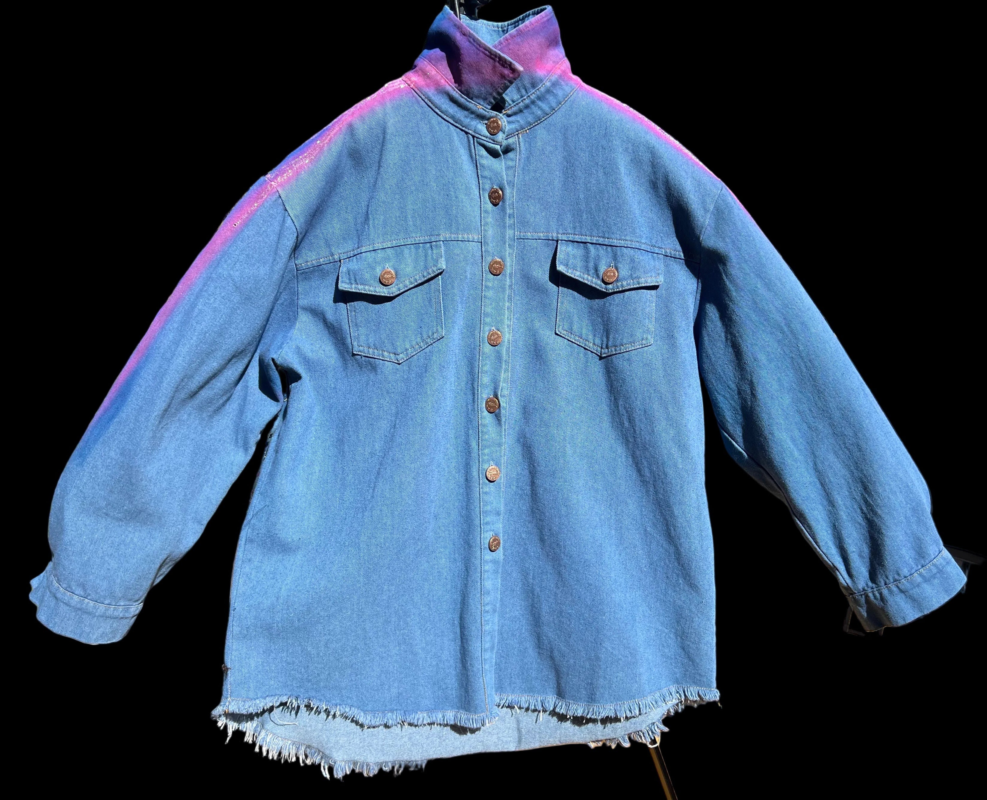 Blue denim Loria NYC Art jacket on a hanger with a blurred outdoor background