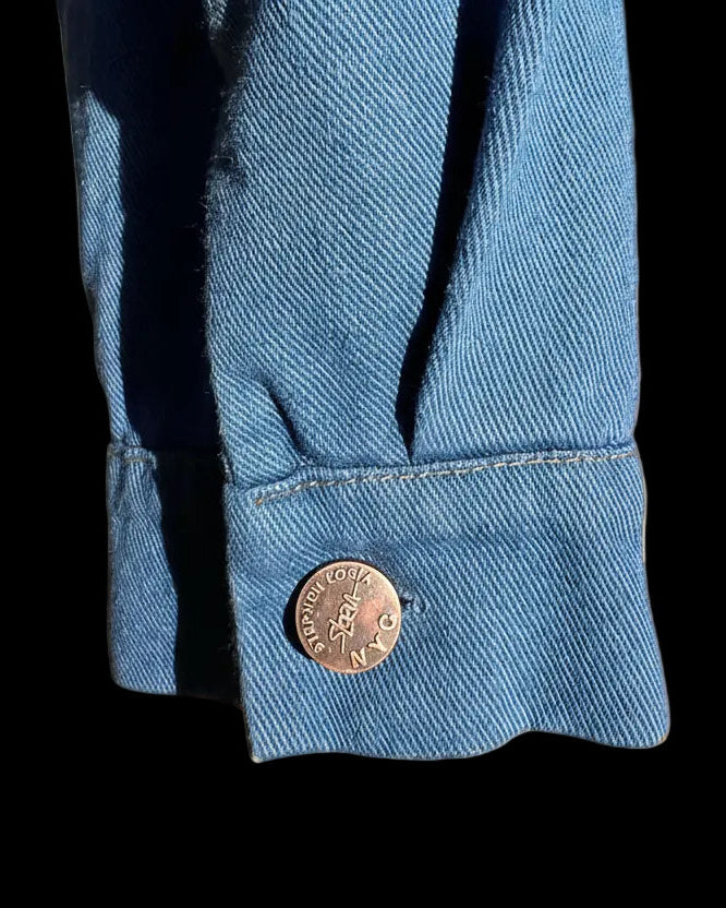 Loria NYC Art Close-up of a blue denim cuff with a button on a black background 