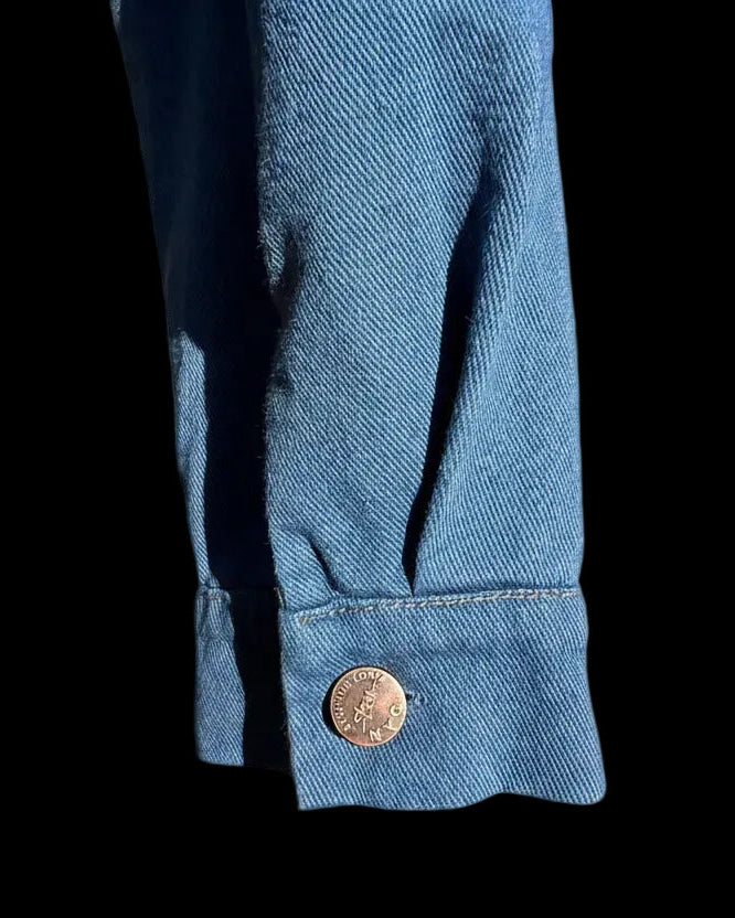 Close-up of a blue denim cuff with a Loria NYC Art button on grey background 