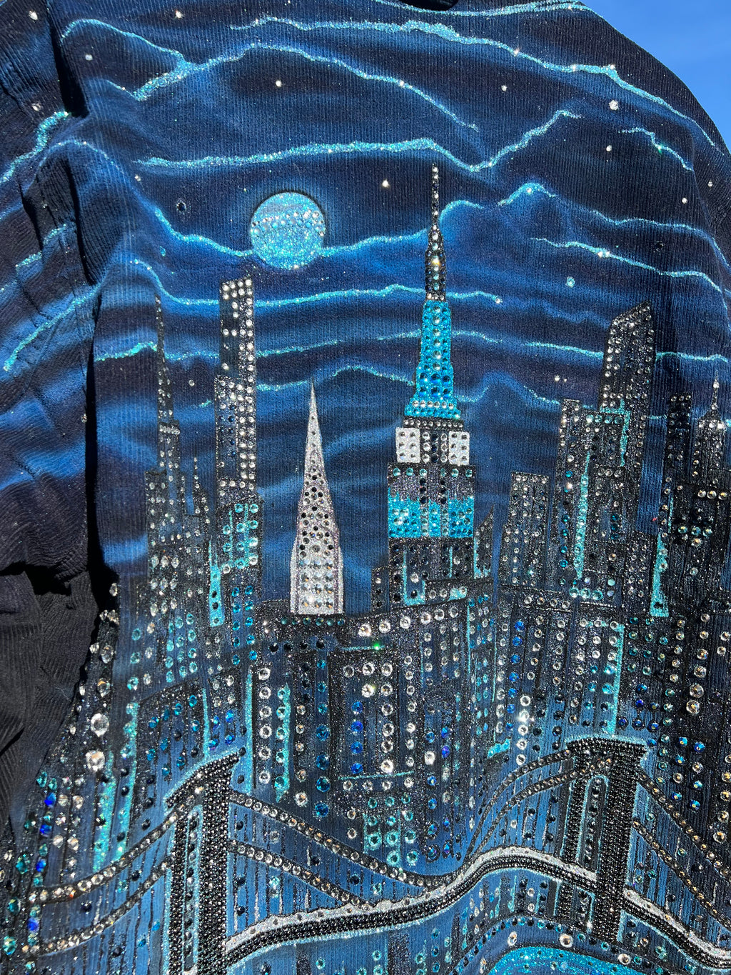Close-up of a blue and silver cityscape themed jacket with painted Loria NYC Art design.