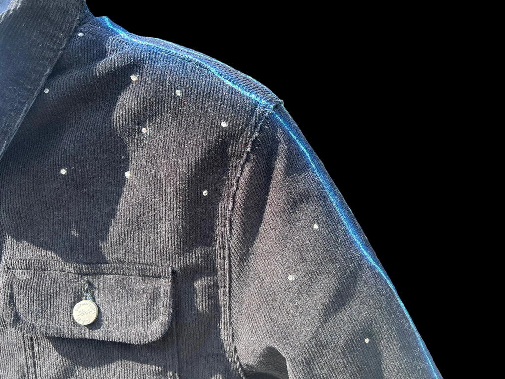 Close-up of a dark denim jacket with white buttons against a blurred natural background