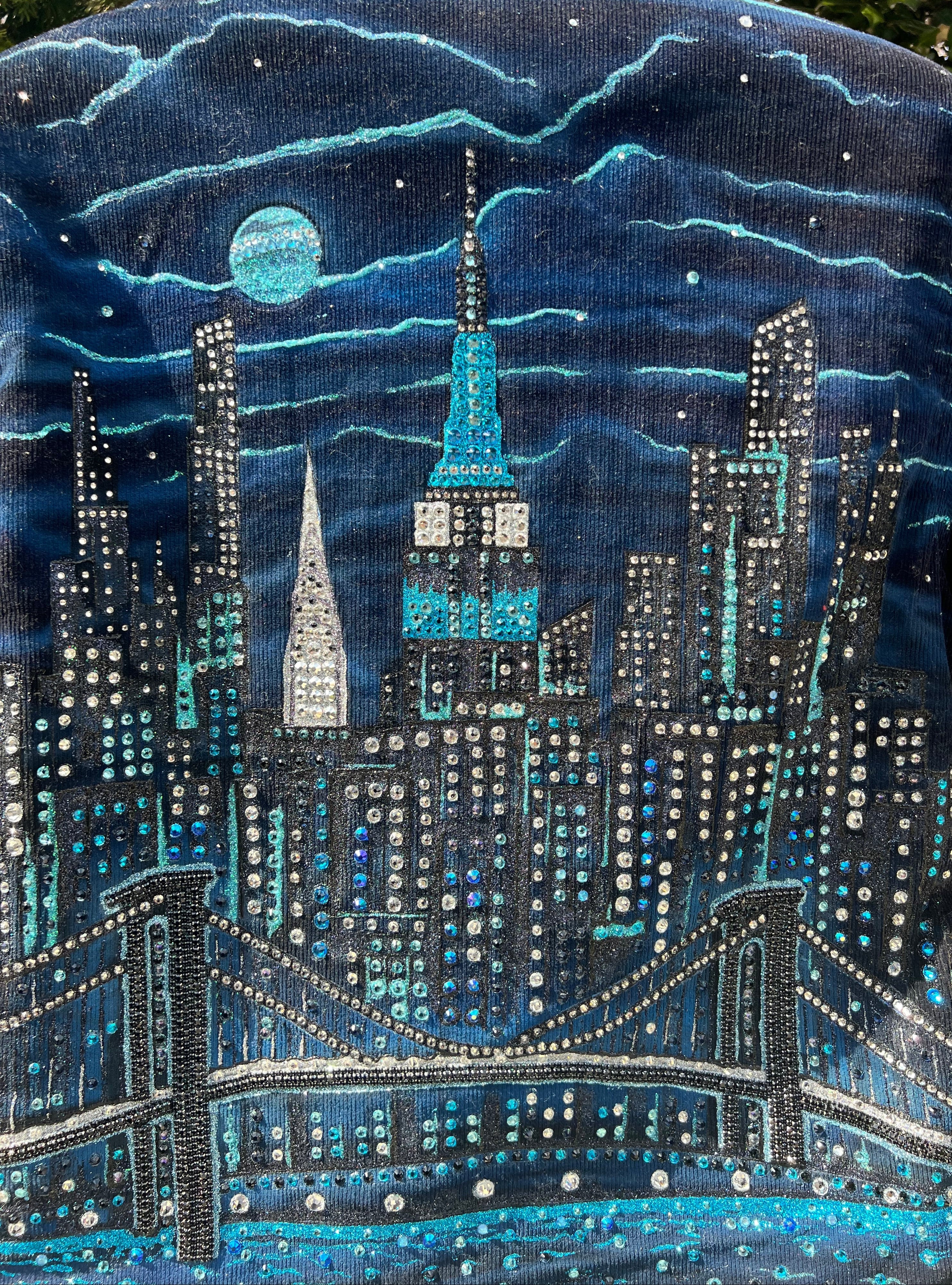 Close-up of a detailed embroidered design on fabric, featuring Loria NYC Art patterns and blue accents.