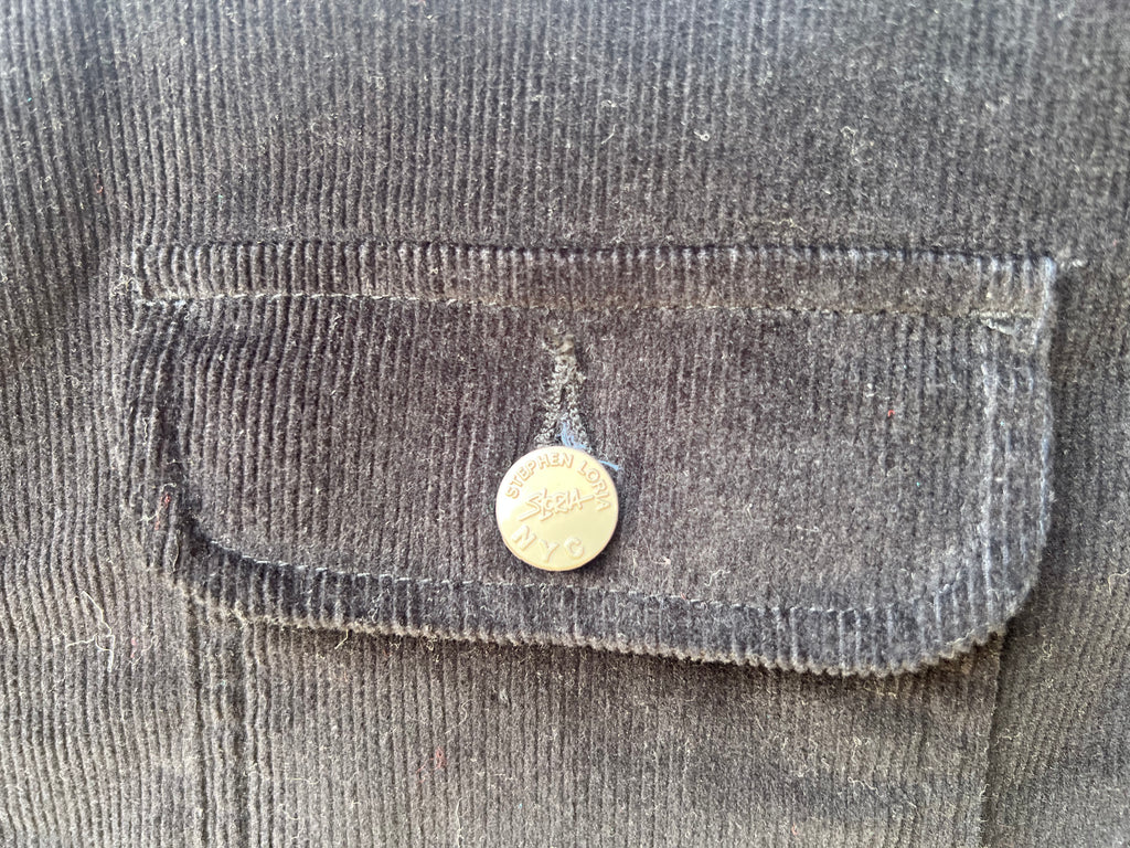Close-up of a pocket on a dark jacket with a Loria NYC Art button.