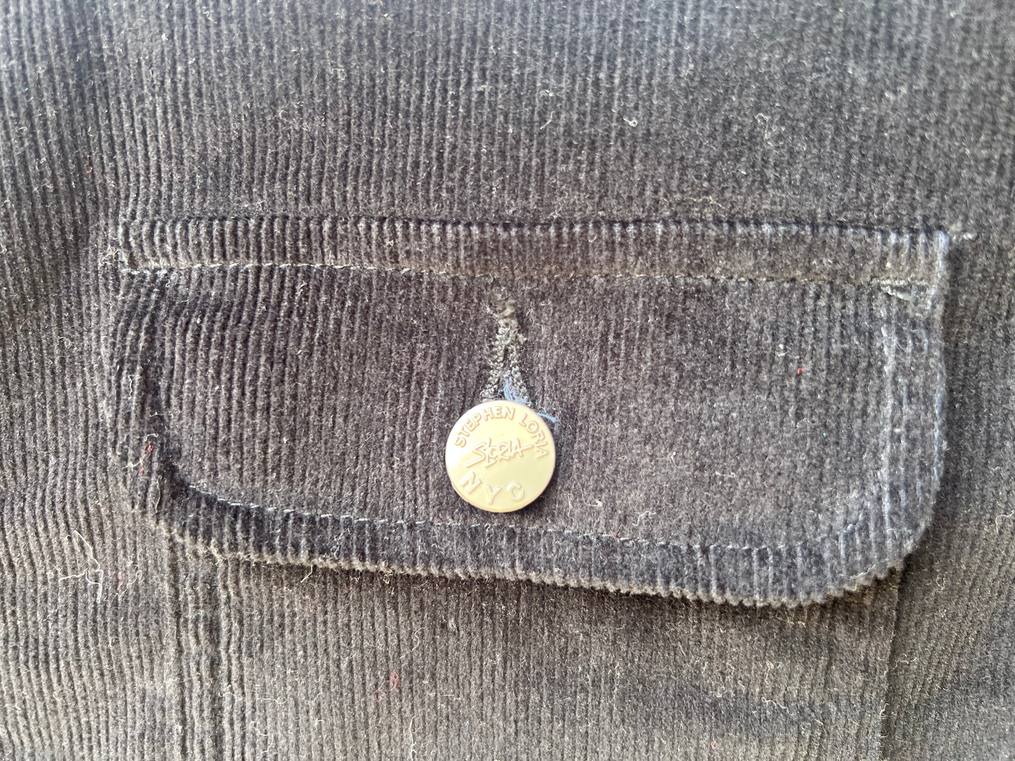 Close-up of a pocket on a dark jacket with a Loria NYC Art button.