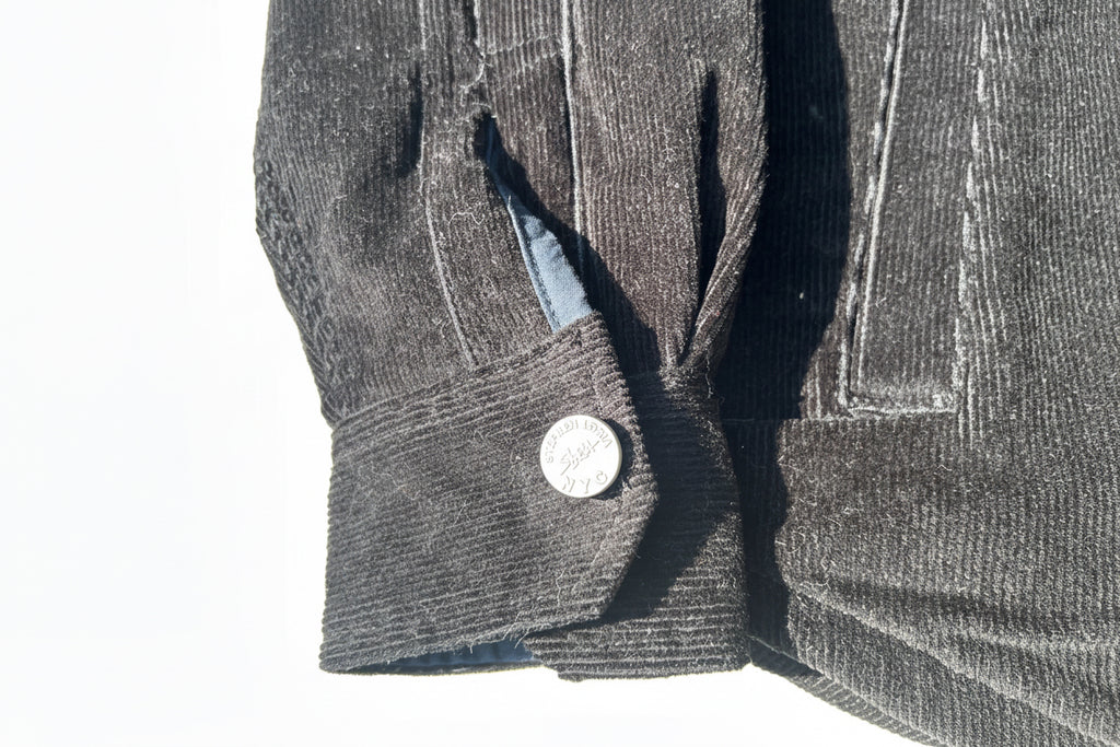 Close-up of a gray textured fabric with a Loria NYC Art button on a reflective surface