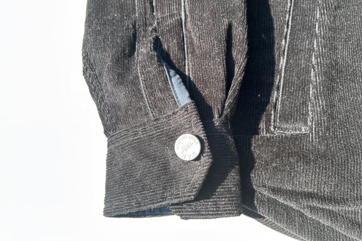 Close-up of a gray textured fabric with a Loria NYC Art button on a reflective surface