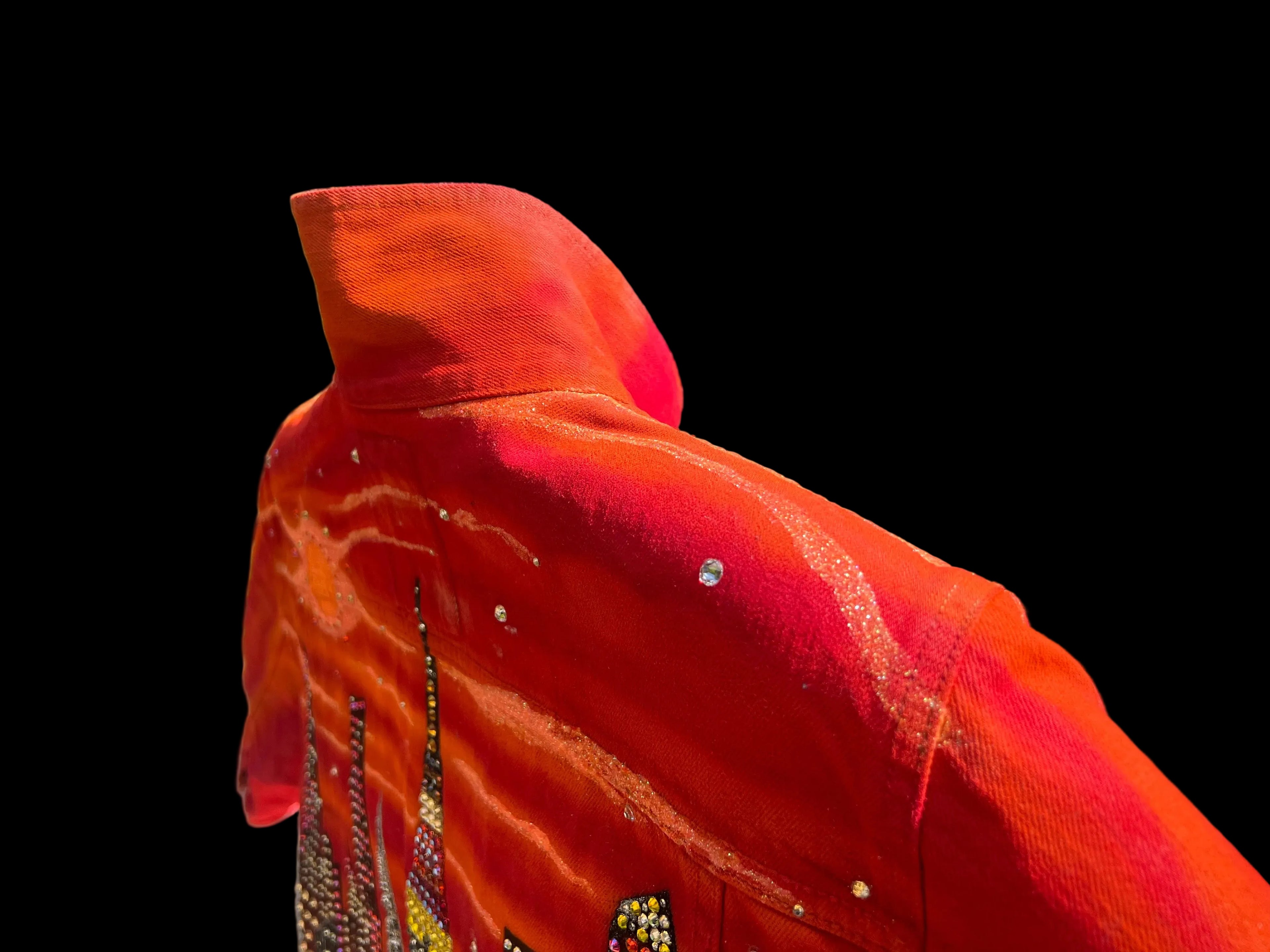 Close-up of a orange garment with decorative Loria NYC Art on a black background 