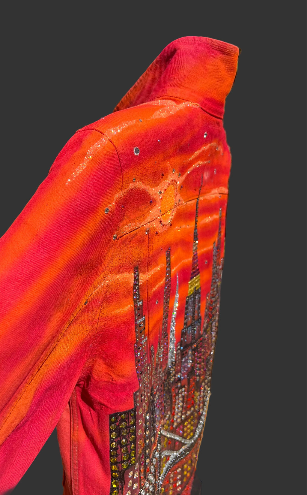 Close-up of a orange jacket with intricate Loria NYC Art on a grey background