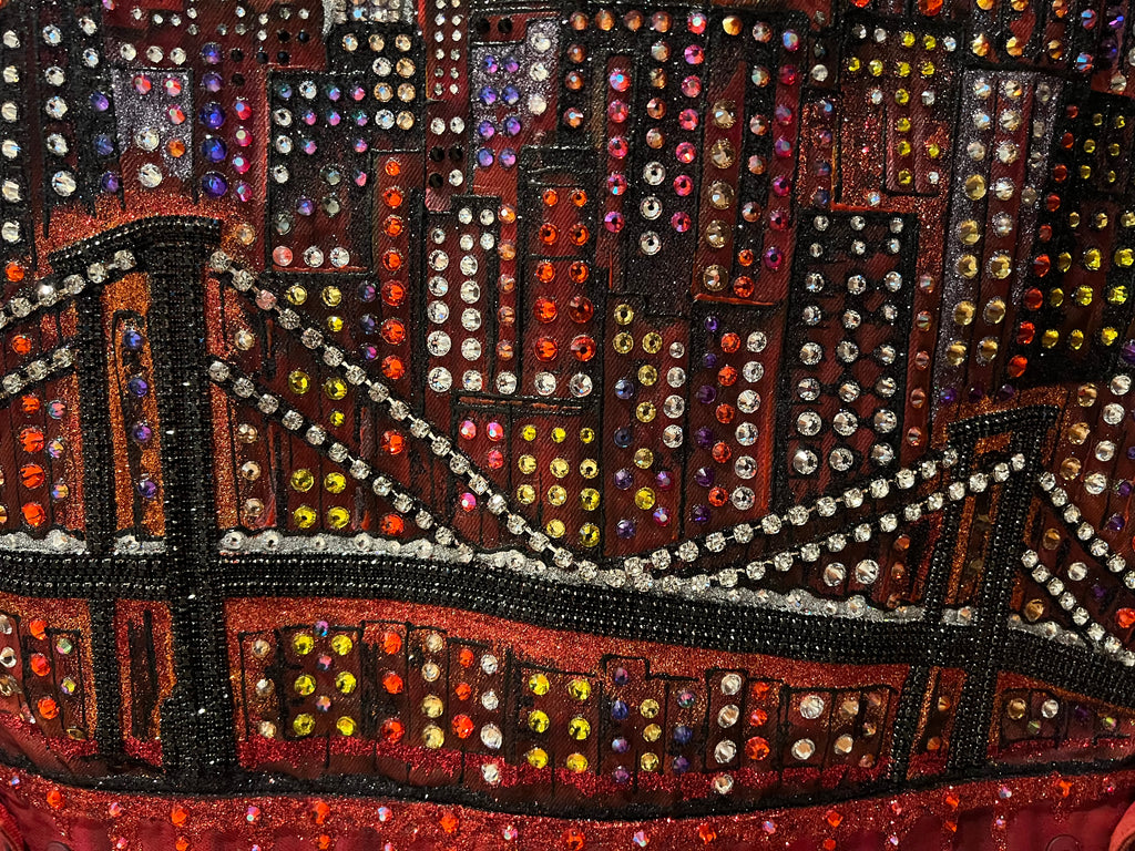 Close-up of a beaded or embroidered fabric with a cityscape Loria NYC Art design featuring a bridge.