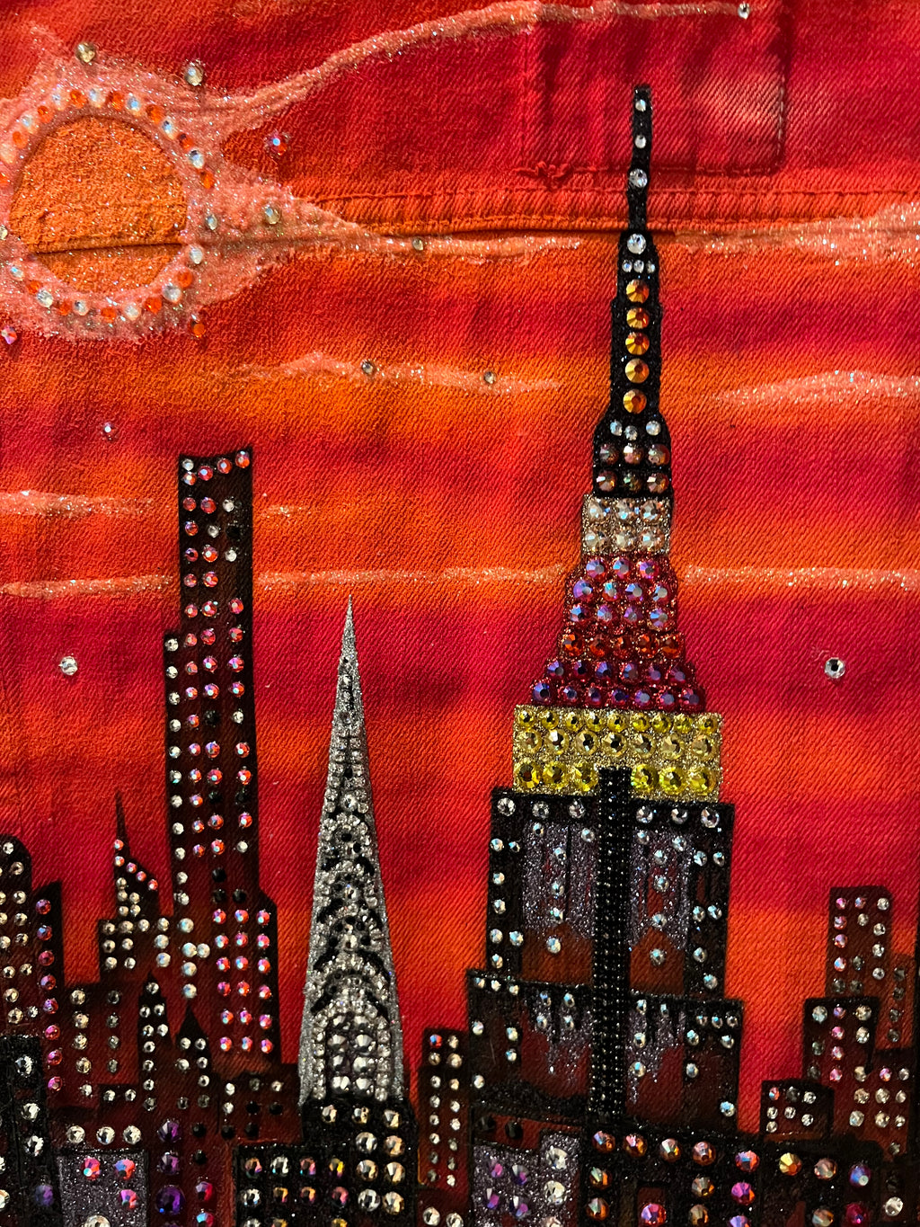Decorative Loria NYC Art with gemstones on a orange fabric background
