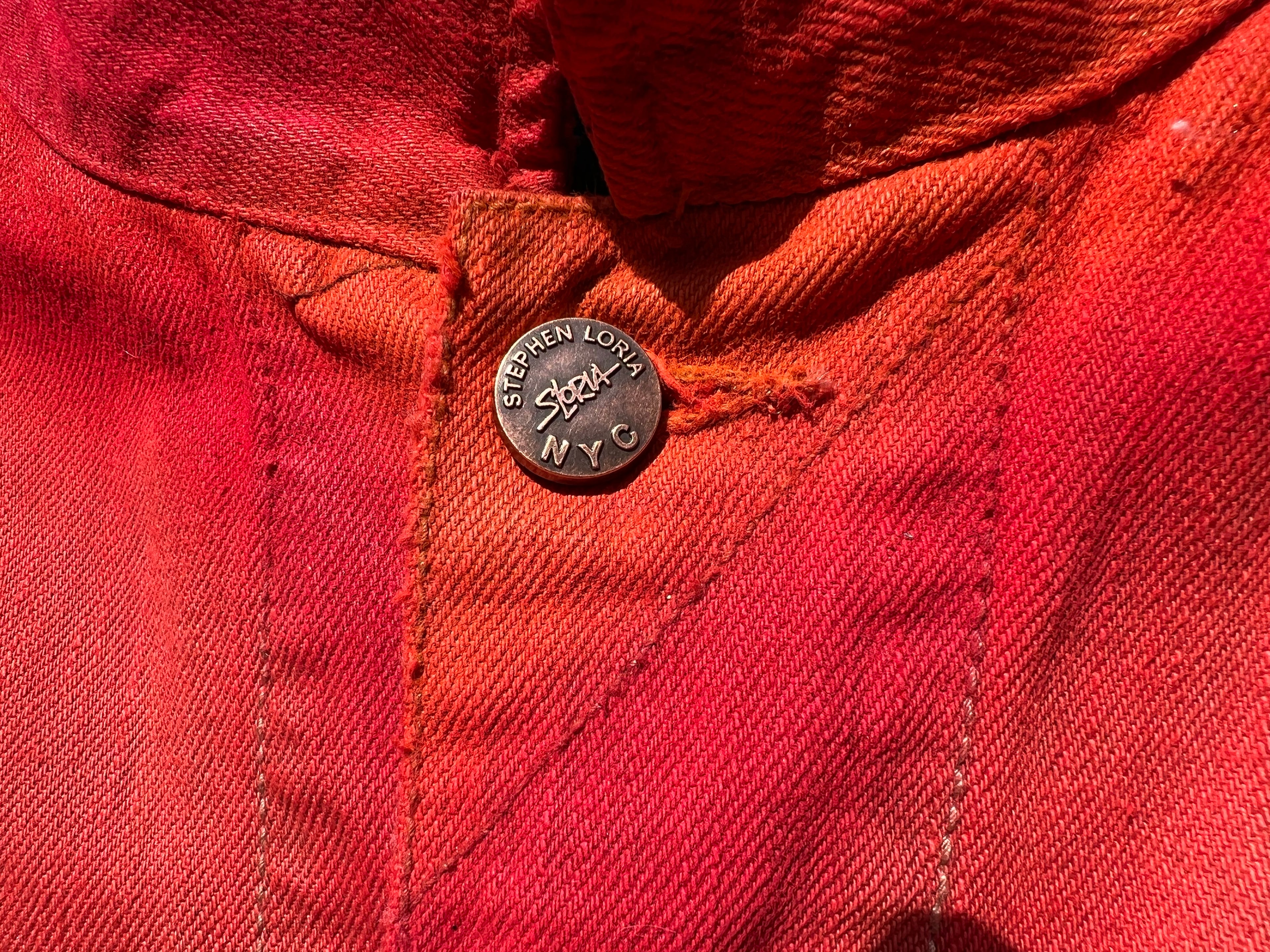 Close-up of a red jacket with a button featuring 'Stephen Loria' branding.