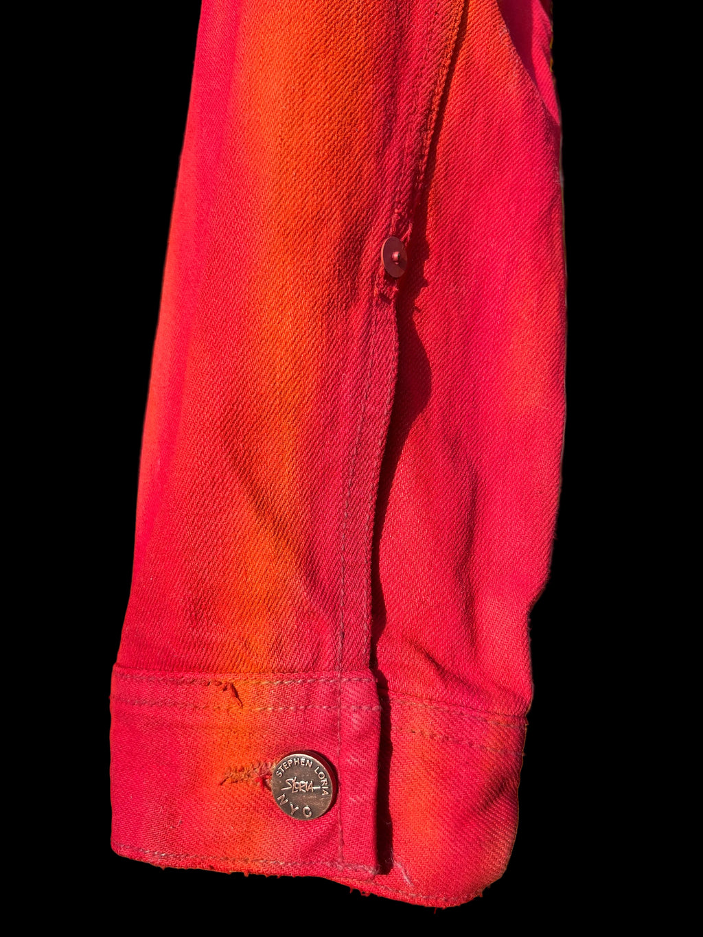 Close-up of a red shirt sleeve with a  Loria NYC Art button, black background