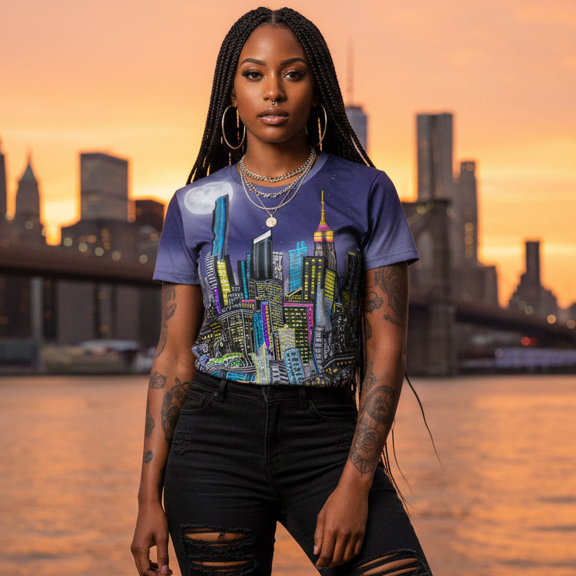 Woman wearing a colorful Loria NYC Art cityscape t-shirt with a city skyline and sunset in the background
