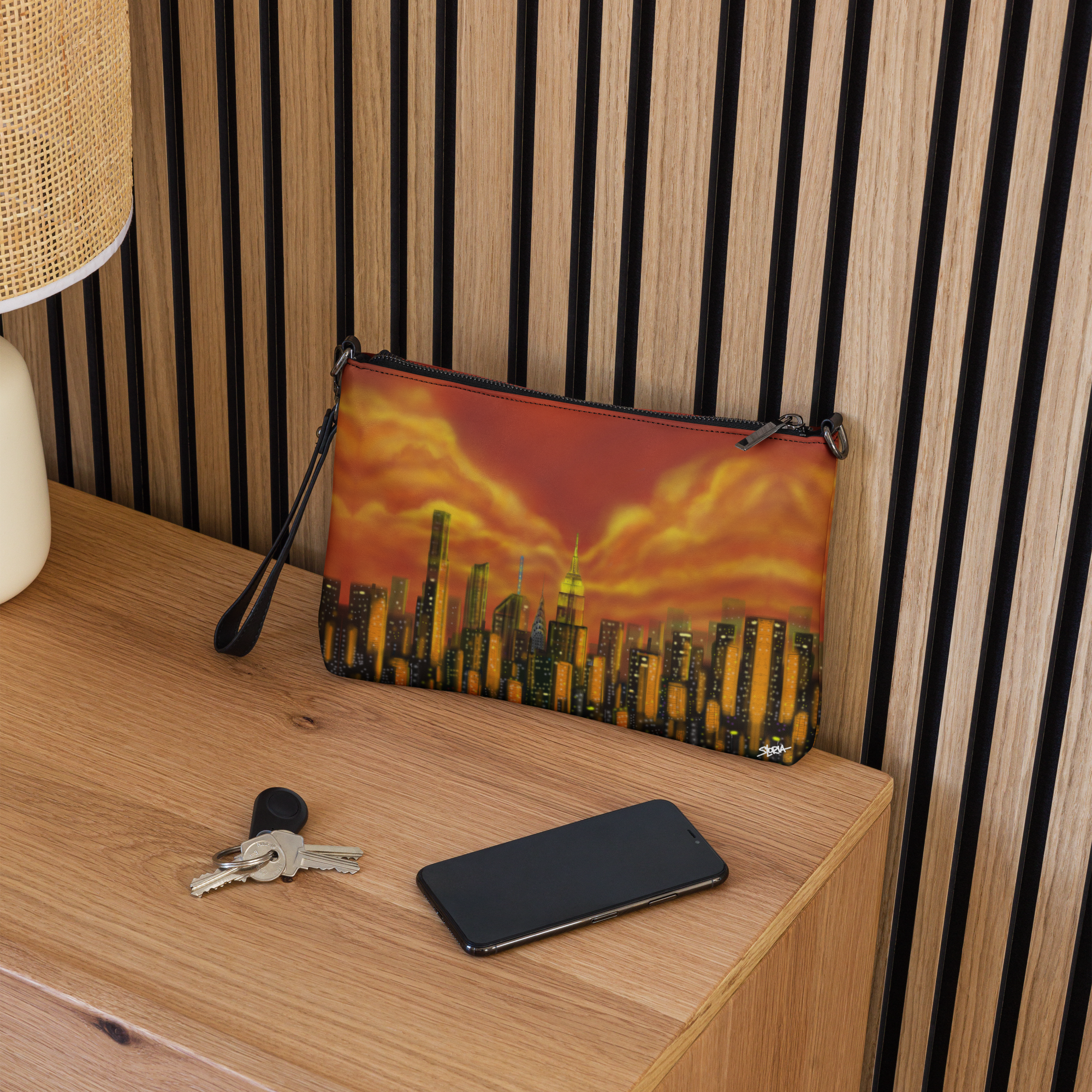 Clutch bag with Loria NYC Art cityscape design on a wooden surface with keys and phone