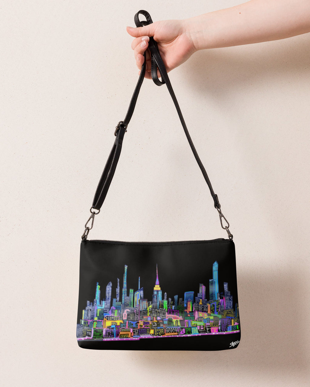 Black handbag with colorful cityscape design held by a hand against a beige background