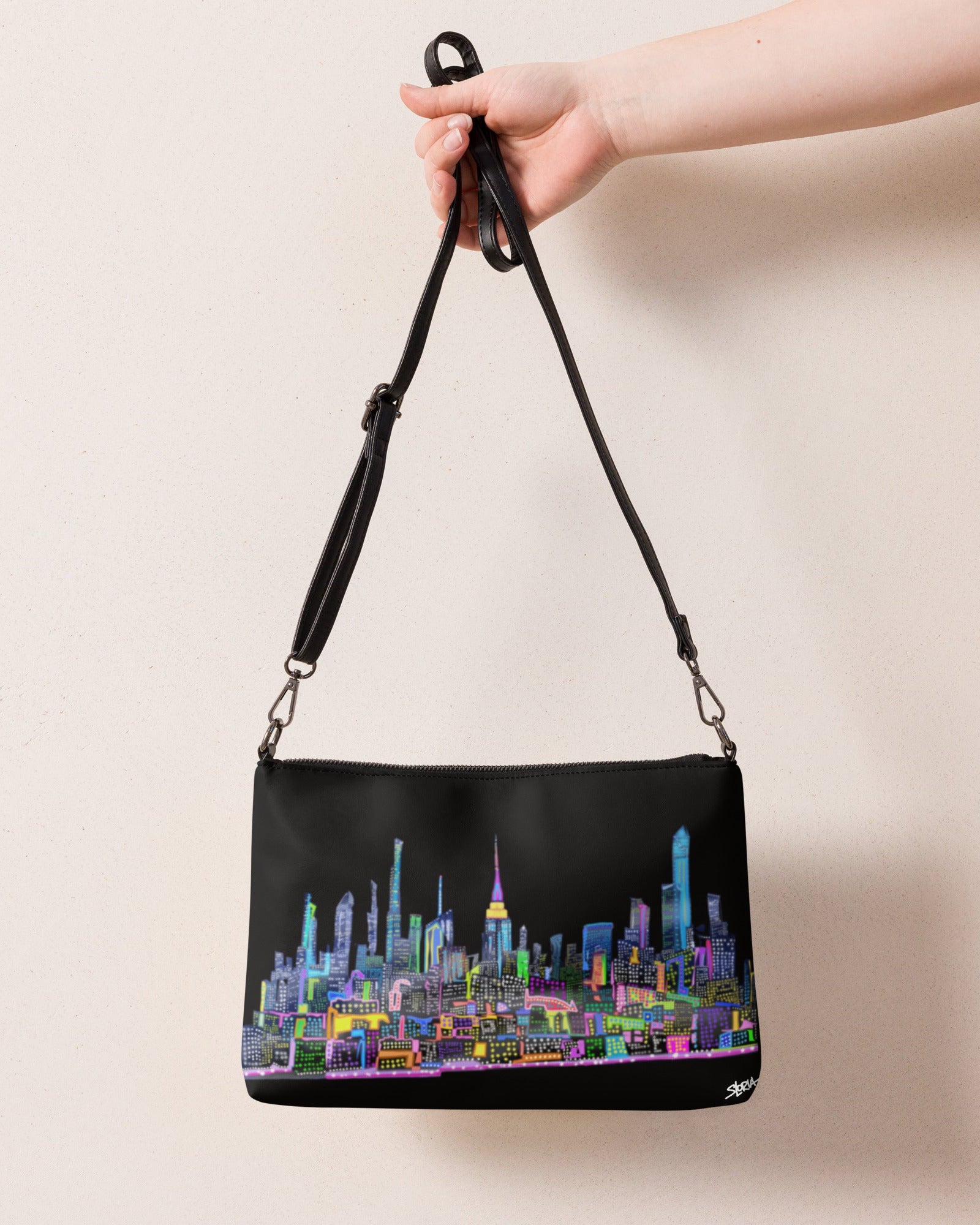 Black handbag with colorful cityscape design held by a hand against a beige background