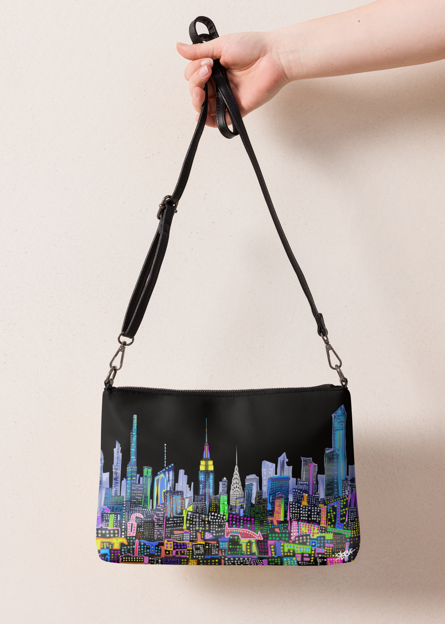 Black handbag with colorful Loria NYC Art cityscape design held by a hand against a beige background