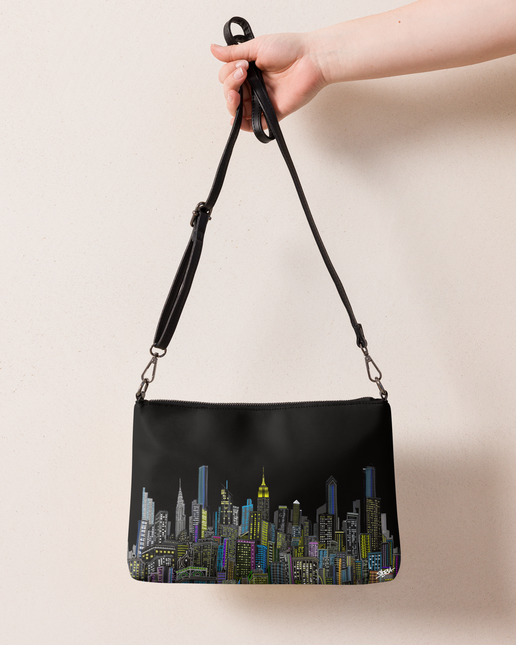 Black handbag with cityscape Loria NYC Art design held by a hand against a beige background