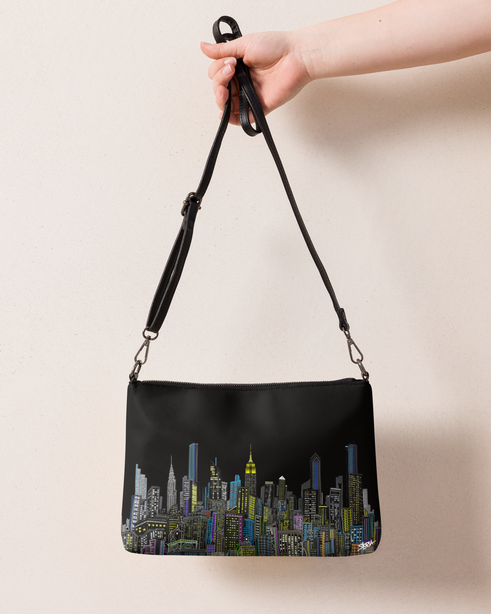 Black handbag with cityscape Loria NYC Art design held by a hand against a beige background