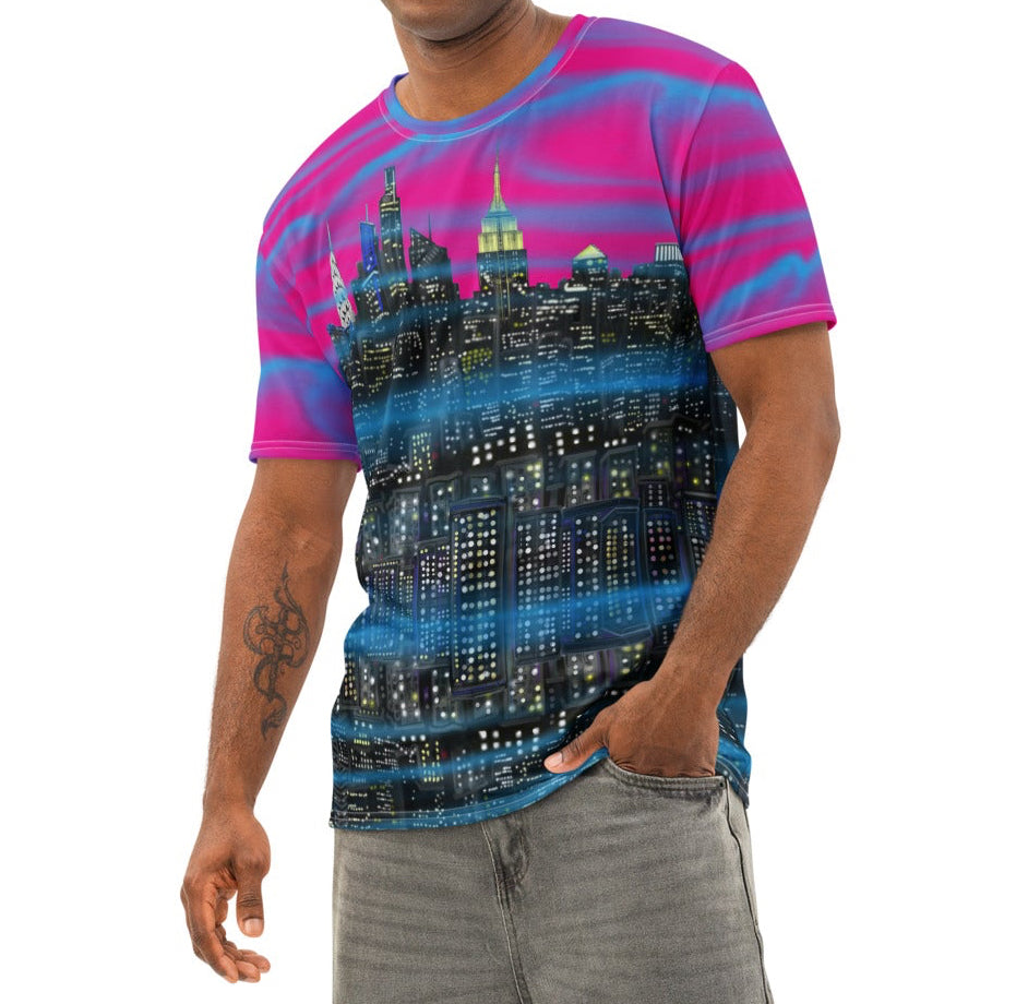 Man wearing a colorful Loria NYC Art t-shirt and gray pants standing in a bright room with large windows.