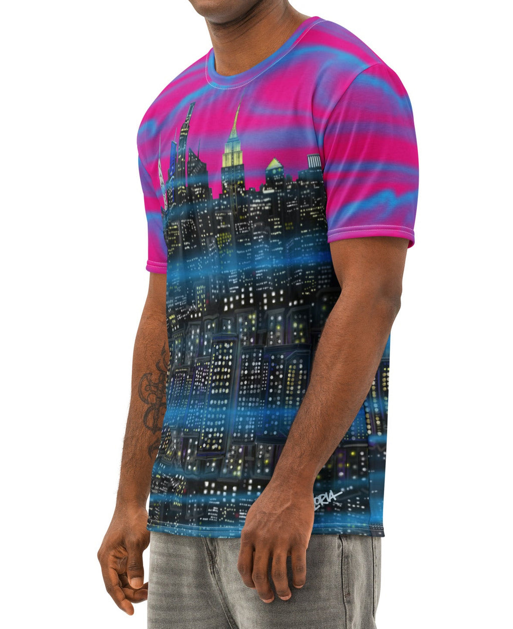 Man wearing a Loria NYC Art colorful shirt with a cityscape design, standing on a rooftop with a city skyline in the background during sunset.