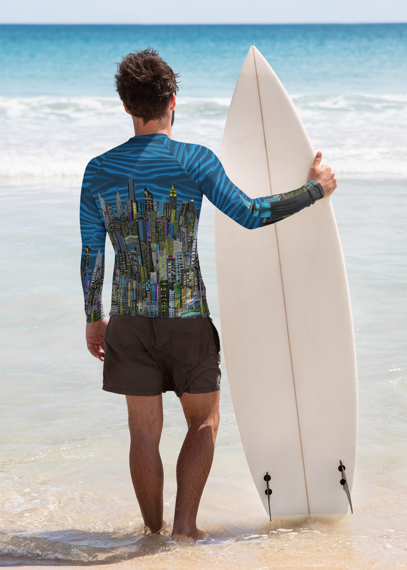 Man wearing a  Loria NYC Art rash guard shirt holding a surfboard on a beach with clear blue water
