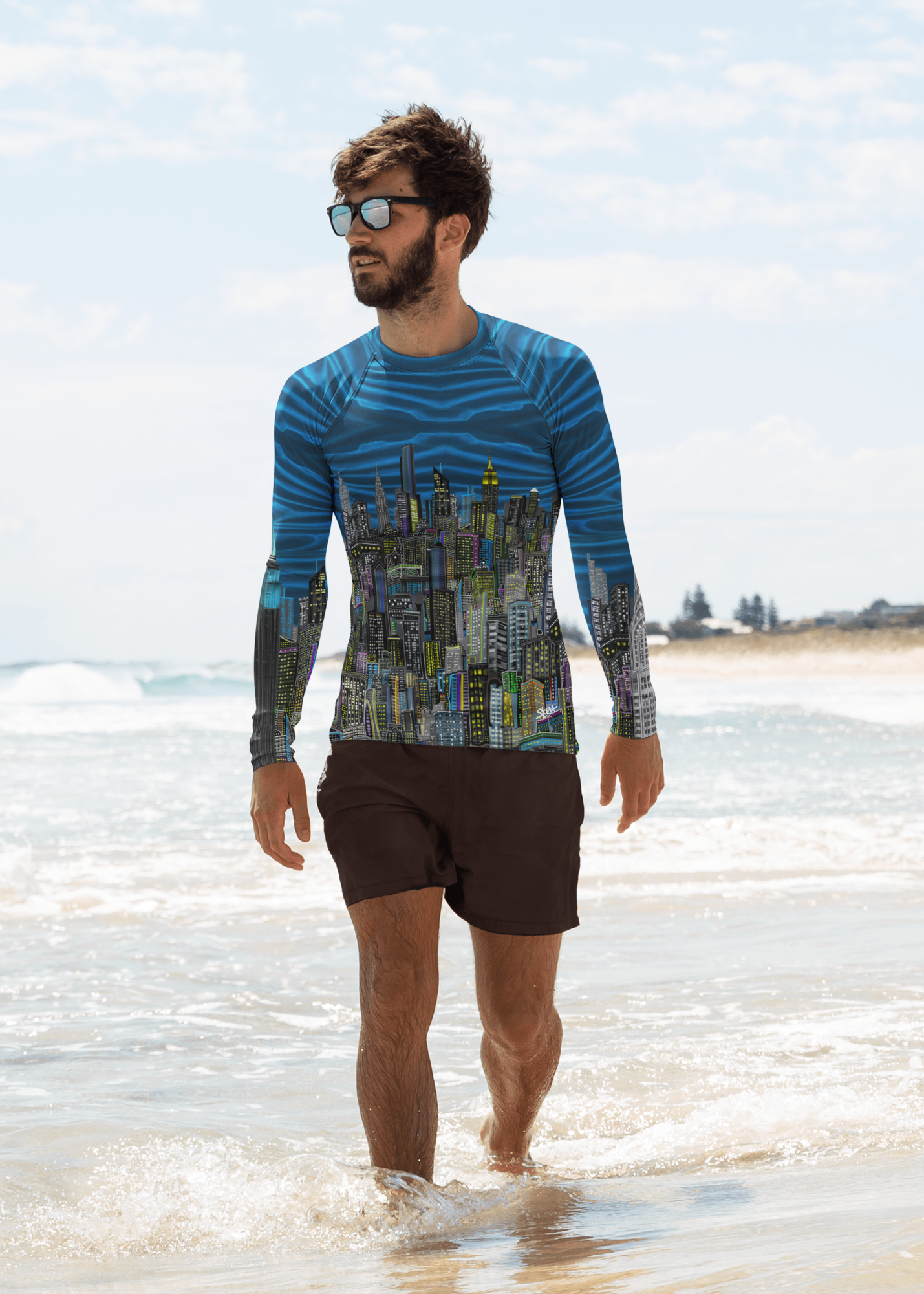 Man wearing a blue patterned long-sleeve  Loria NYC Art shirt and sunglasses on a beach.