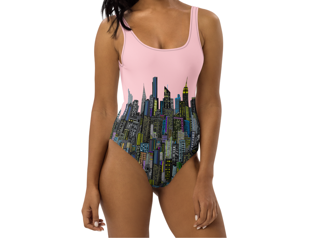 Woman wearing a pink Loria NYC Art one-piece swimsuit with cityscape design on a white background