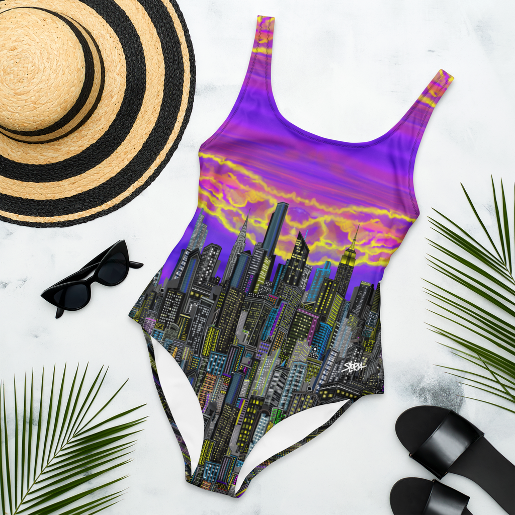 One-piece swimsuit with Loria NYC Art cityscape design, sun hat, sunglasses, and sandals on a white background