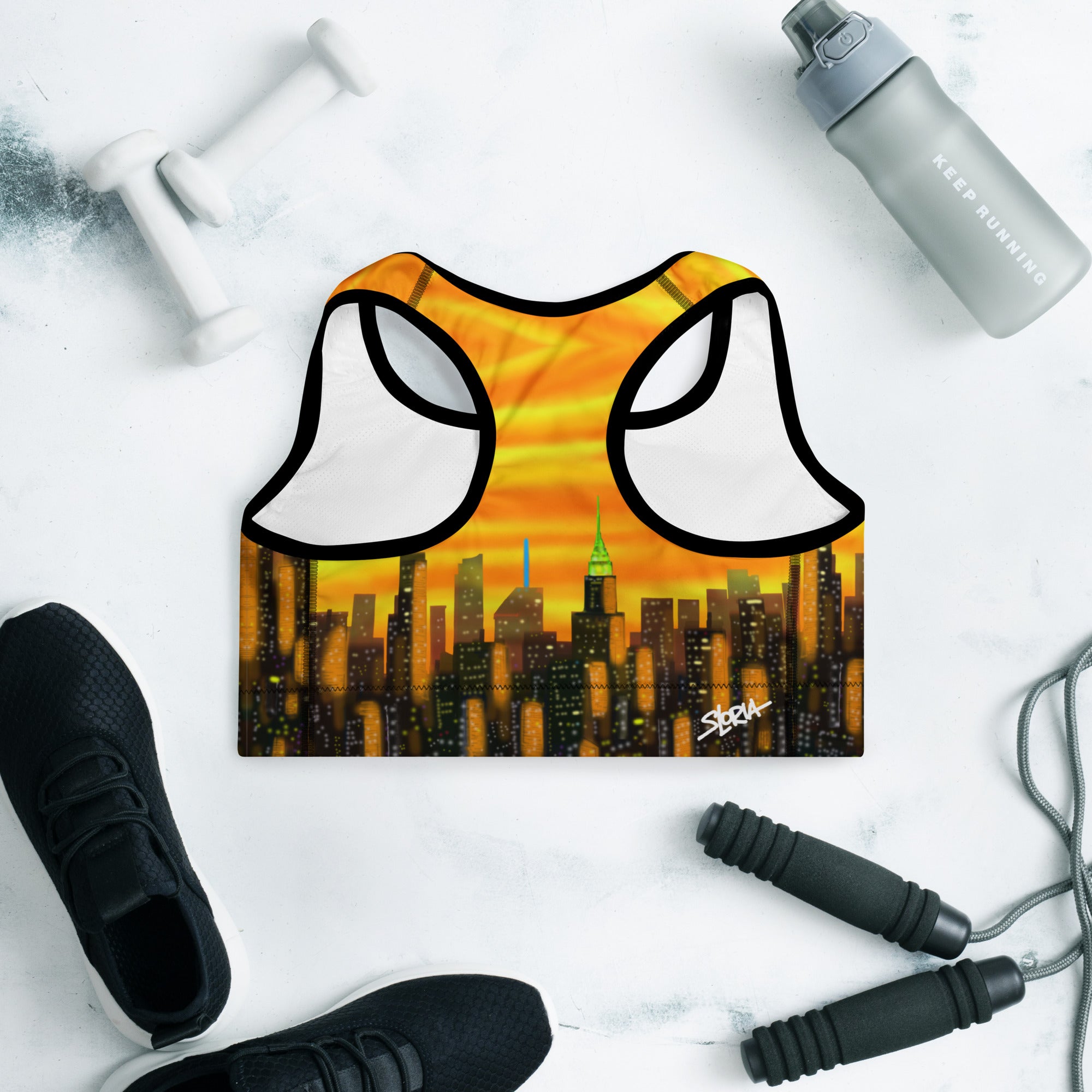 Sports bra with cityscape design by Loria NYC Art on a white surface with gym equipment.