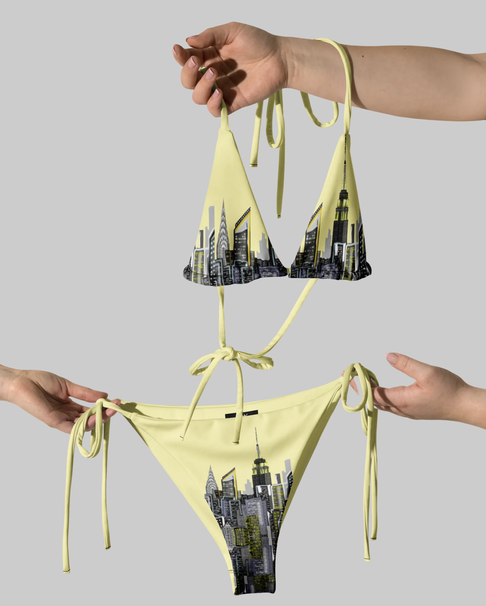 Yellow bikini with Loria NYC Art cityscape design held by hands against a gray background