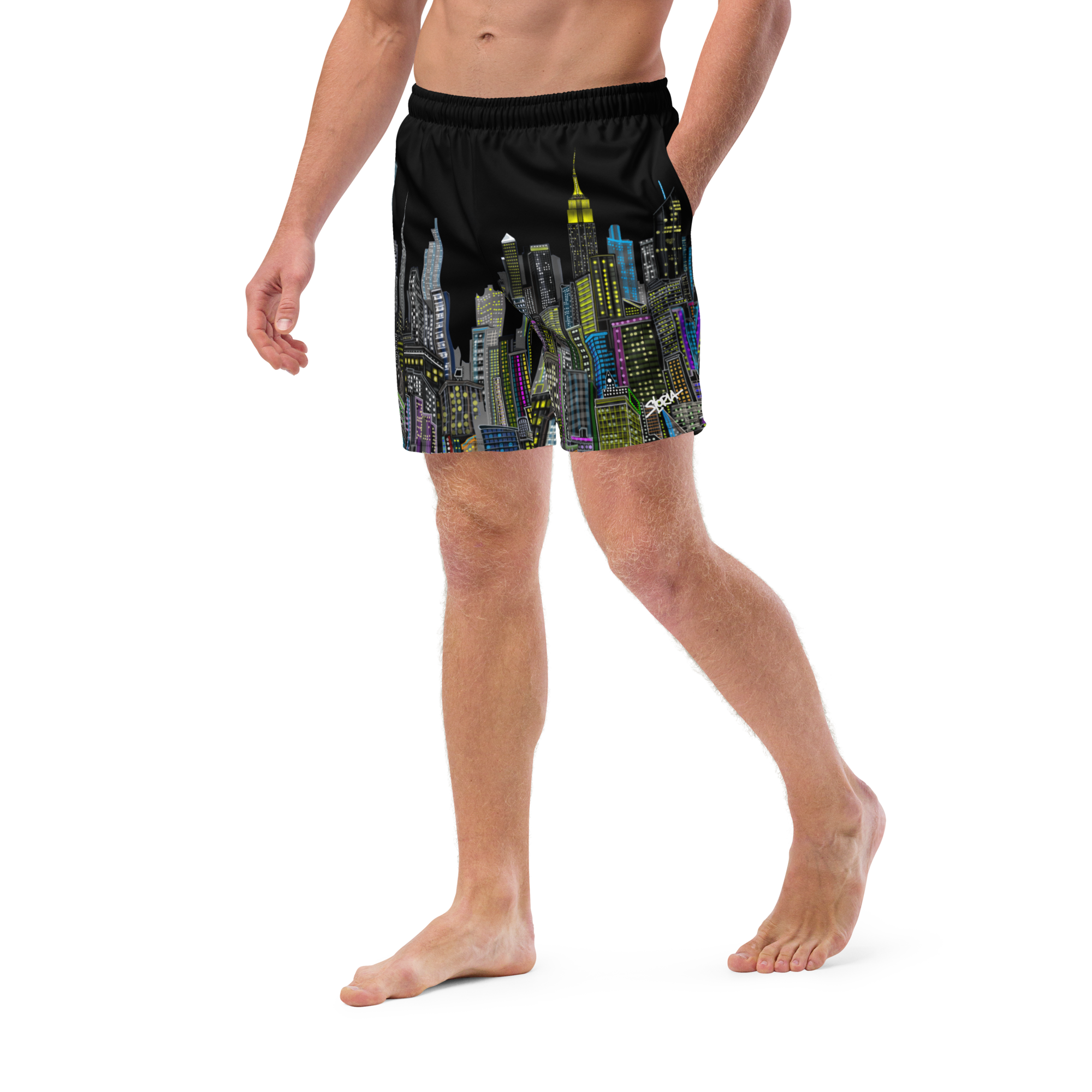 Person wearing black swim Loria NYC Art shorts with colorful cityscape design on a white background