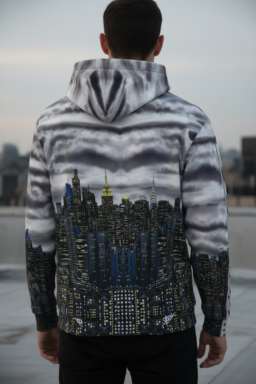 Person wearing a hoodie with aLoria NYC Art cityscape design, standing on a rooftop with a city skyline in the background.