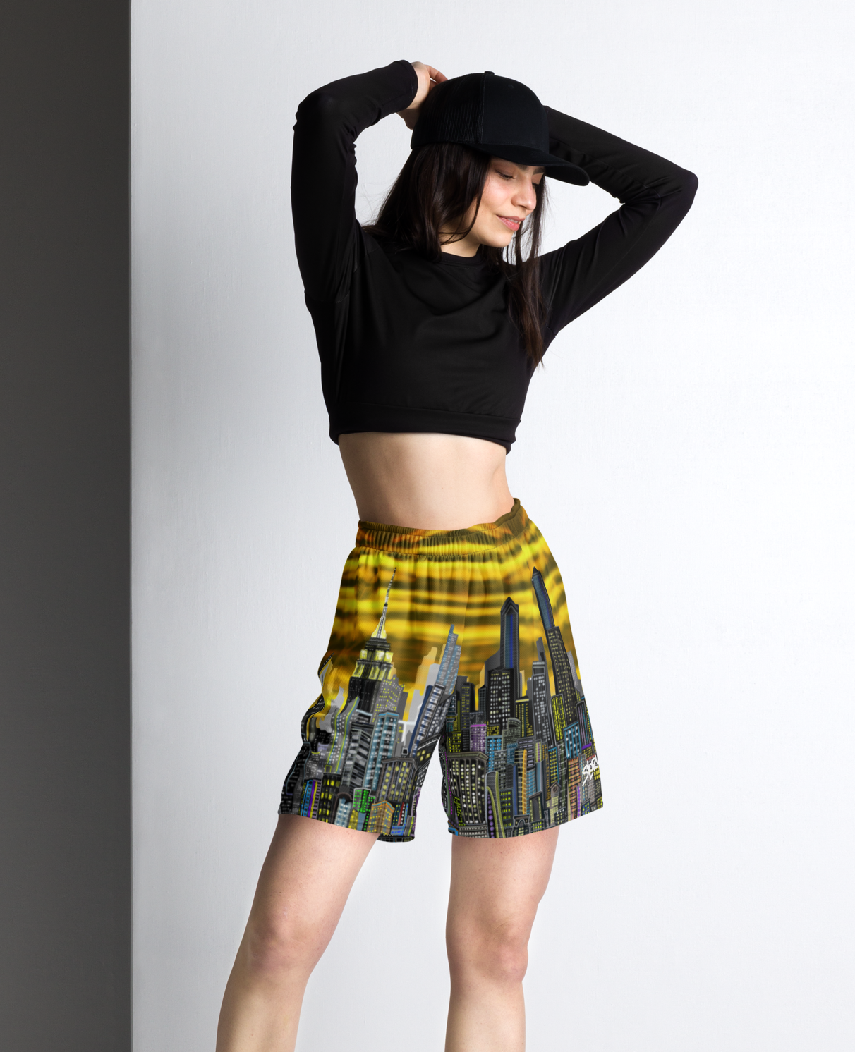 Woman wearing a black crop top and patterned Loria NYC Art shorts against a white wall.