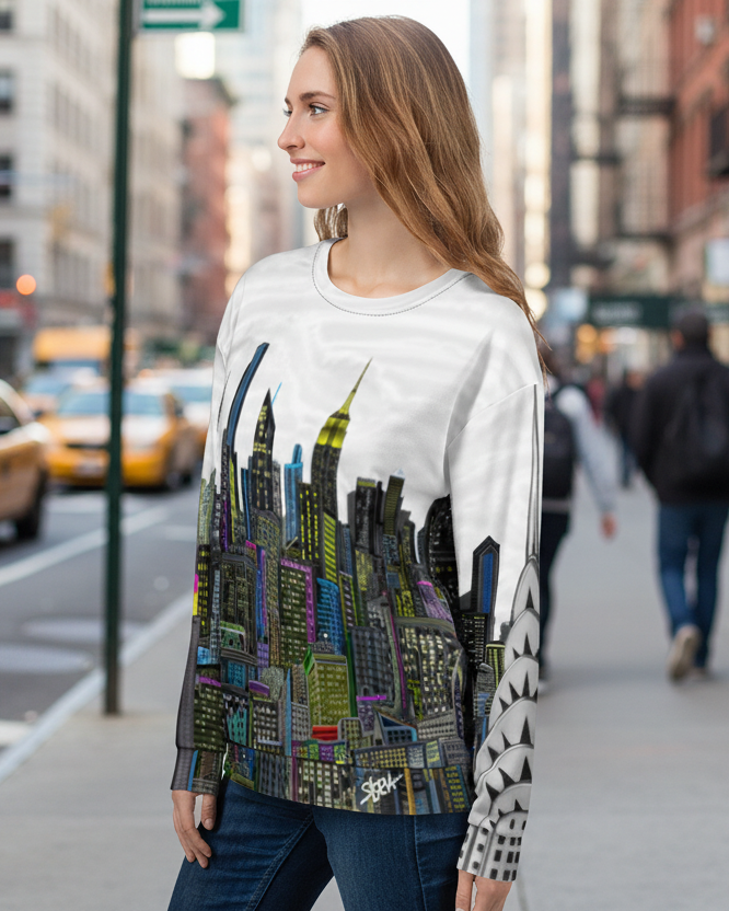 Woman wearing a cityscape Loria NYC Art sweatshirt on a city street with taxis and pedestrians.