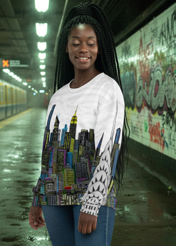 Woman wearing a Loria NYC Art white sweat shirt standing in a subway station with graffiti on the wall