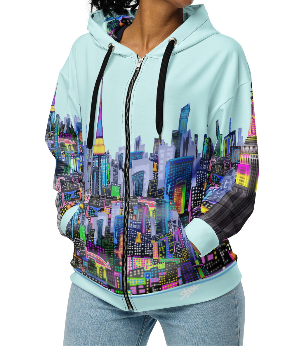 Woman wearing a Loria NYC Art hoodie with a colorful cityscape design on a white background