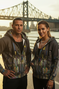 Two people wearing matching Loria NYC Art hoodies with a bridge and river in the background